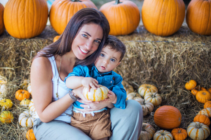 mom pumpkin picking with son with pumpkins in the background